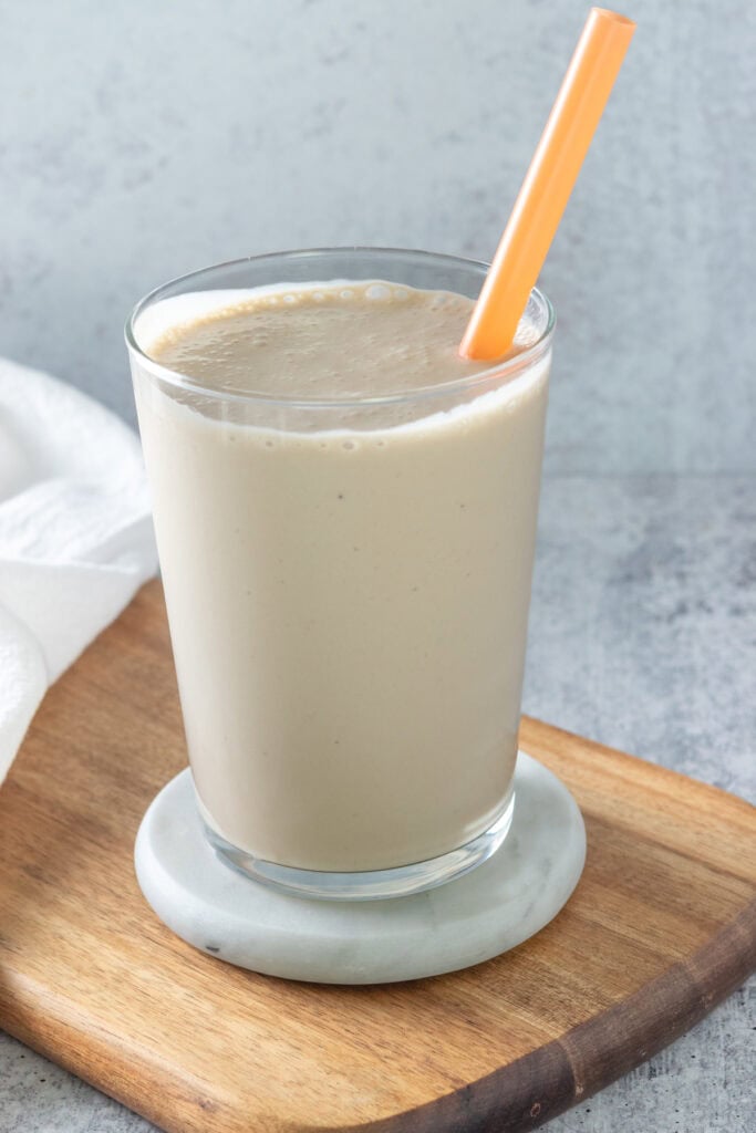 Coffee Banana Smoothie poured into a drinking glass, with a straw inserted into the drink.
