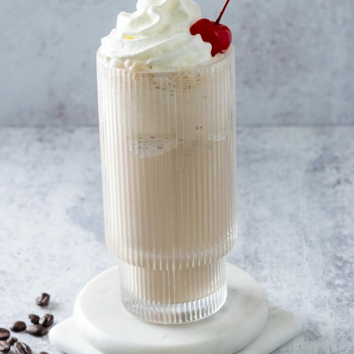 Coffee Milkshake in a tall glass topped with whipped cream and a cherry.