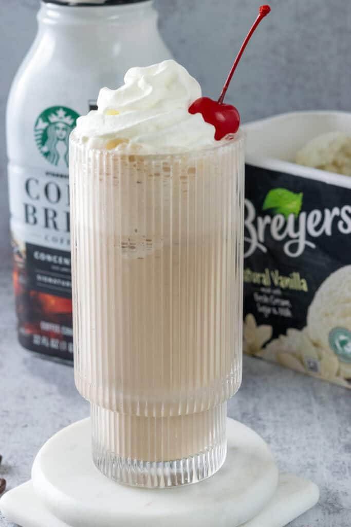 A homemade coffee milkshake topped with whipped cream and a cherry in front of a bottle of Starbucks cold brew coffee concentrate and a carton of Breyers vanilla ice cream.