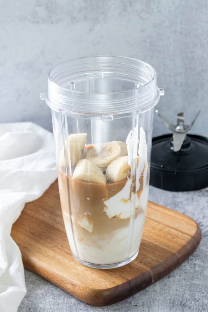A blender cup filled with all the ingredients needed to make a homemade coffee banana smoothie.