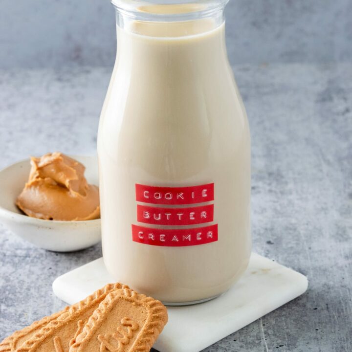 Bottle of homemade cookie butter coffee creamer next to 3 Lotus Biscoff cookies and a small bowl with cookie butter spread in it.