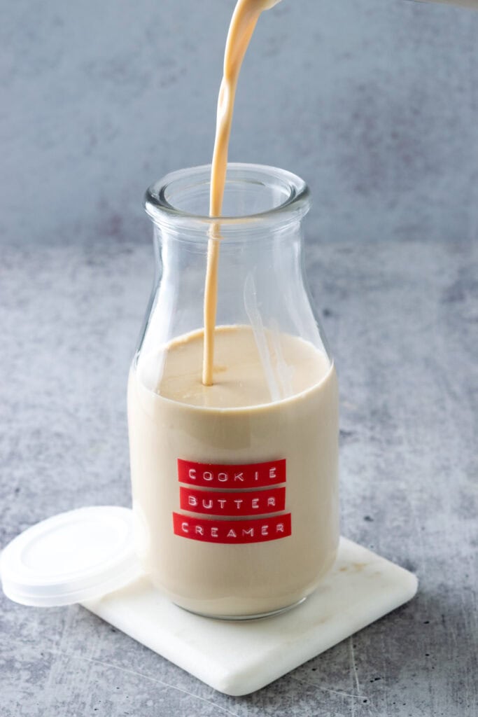 Homemade cookie butter coffee creamer being poured into a small milk bottle with a red label on it that says cookie butter creamer.