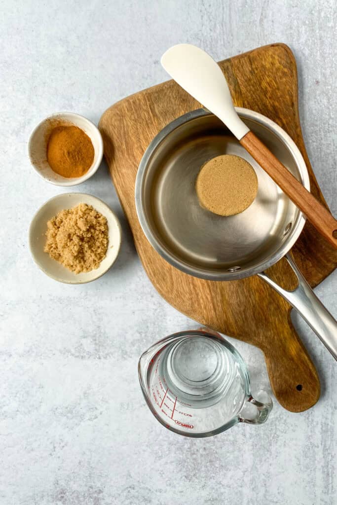 Brown sugar in a saucepan next to a small bowl of brown sugar and another small bowl of cinnamon.