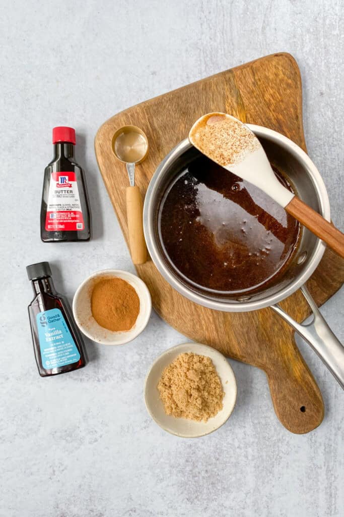 Cinnamon brown sugar simple syrup in a saucepan next to bottles of vanilla and butter extract and small bowls with ground cinnamon and brown sugar.