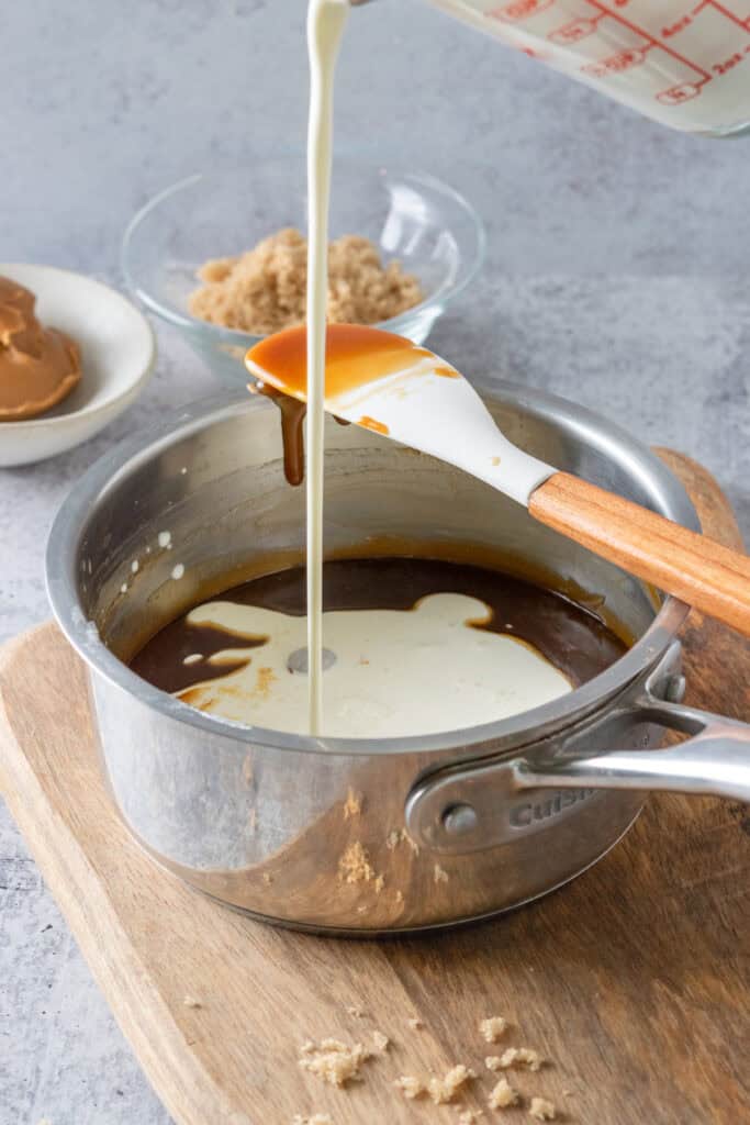 Cream being poured into saucepan that has cookie butter sauce in it.