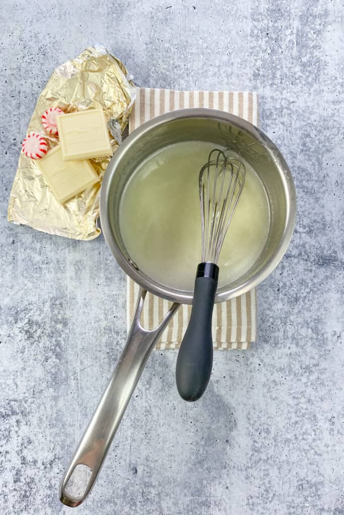 A whisk in the saucepan showing the smooth and creamy white chocolate sauce.