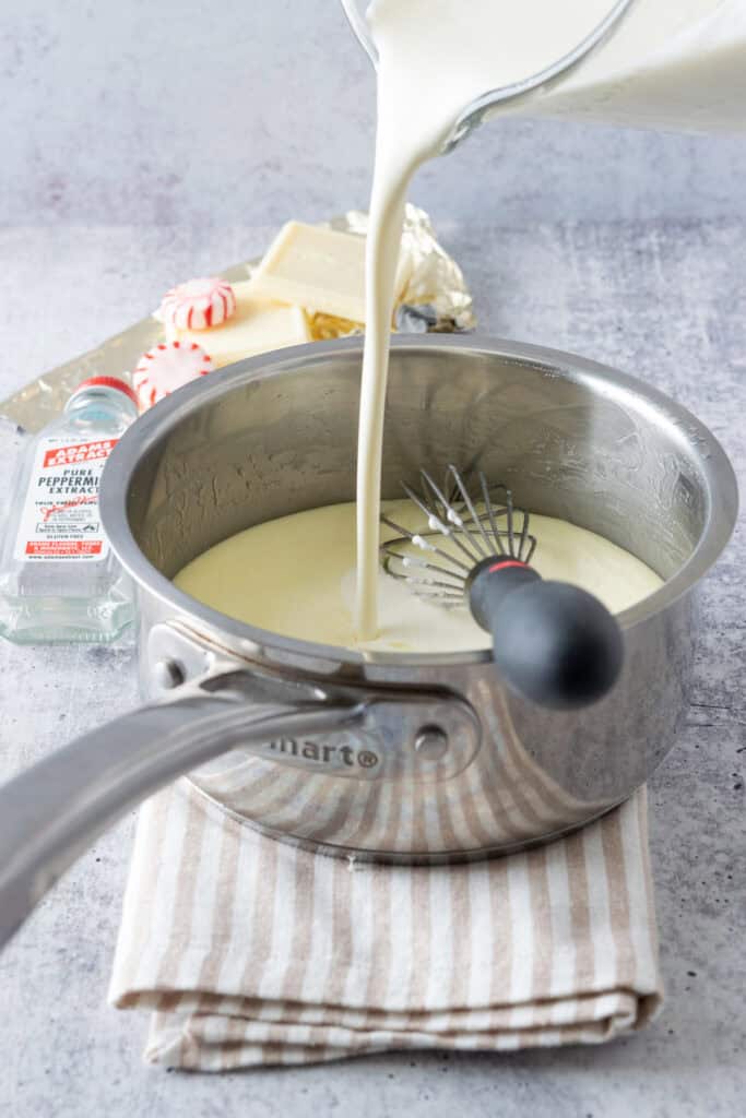 A stream of cream and milk being whisked into the white chocolate sauce, which is next to a bottle of peppermint extract.