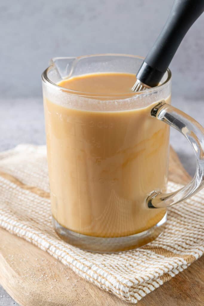 A large glass measuring cup with cream and homemade caramel sauce stirred together to make creamer.