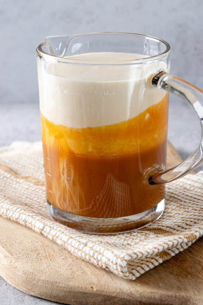 Layers of white cream and golden caramel sauce in a large glass measuring cup before being stirred together to make coffee creamer.