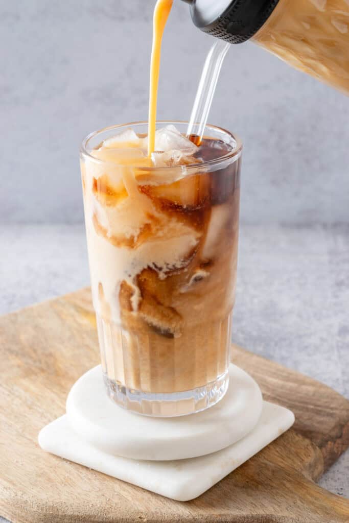 Salted caramel creamer being poured into an iced coffee drink to make an iced salted caramel latte.