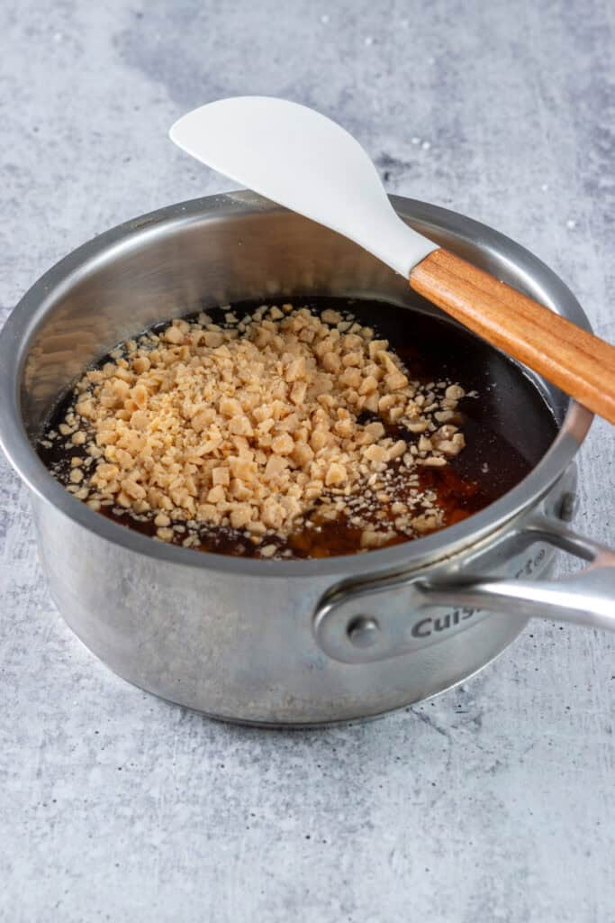 Water and toffee bits added to a small saucepan that has white and brown sugar in it.