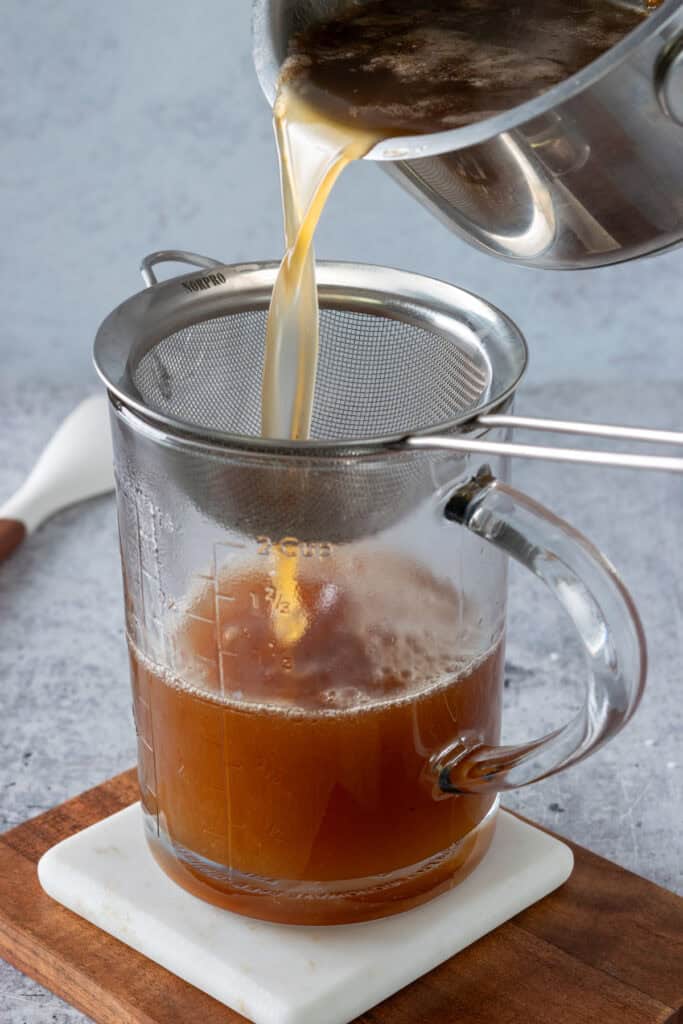 Pouring syrup through a strainer into a glass measuring cup to remove any bits of solid toffee that remains.