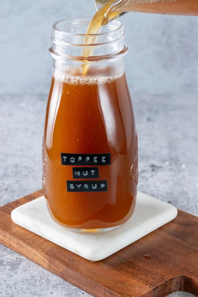 Pouring syrup into a glass bottle that has a label on it that says, toffee nut syrup.